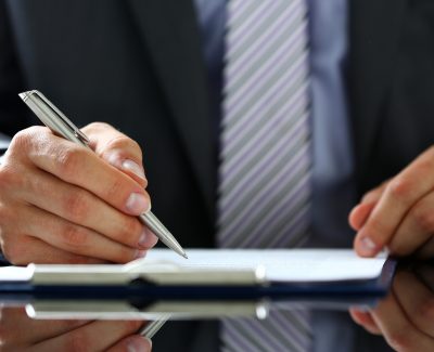 Man in suit and tie pen in hand hovering over a clipboard