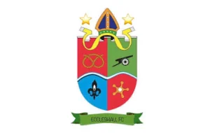 Eccleshall FC club crest featuring a multicolored shield, bishop’s mitre, fleur-de-lis, cannon symbol, and green banner.